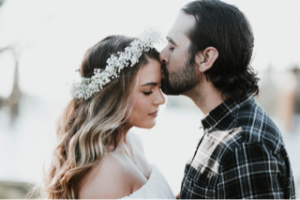 A man in a flannel shirt kissing a bride on the forehead.